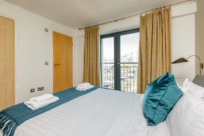 A hotel room with a bed, a window with curtains, a door, and a view of the outside.