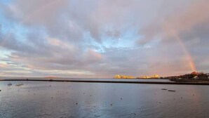 A calm body of water with a rainbow in the sky, a distant shoreline, and a few boats. - Calming Sea View City Apartment (Edinburgh)