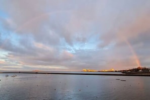 A calm body of water with a rainbow in the sky, a distant shoreline, and a few boats. - Calming Sea View City Apartment (Edinburgh)