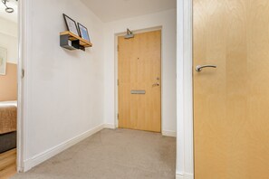 A hallway with a wooden door, a small shelf with framed pictures, and a carpeted floor.