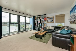 A spacious living room with a large window, a leather sofa, a bookshelf, and a painting. - Calming Sea View City Apartment (Edinburgh)
