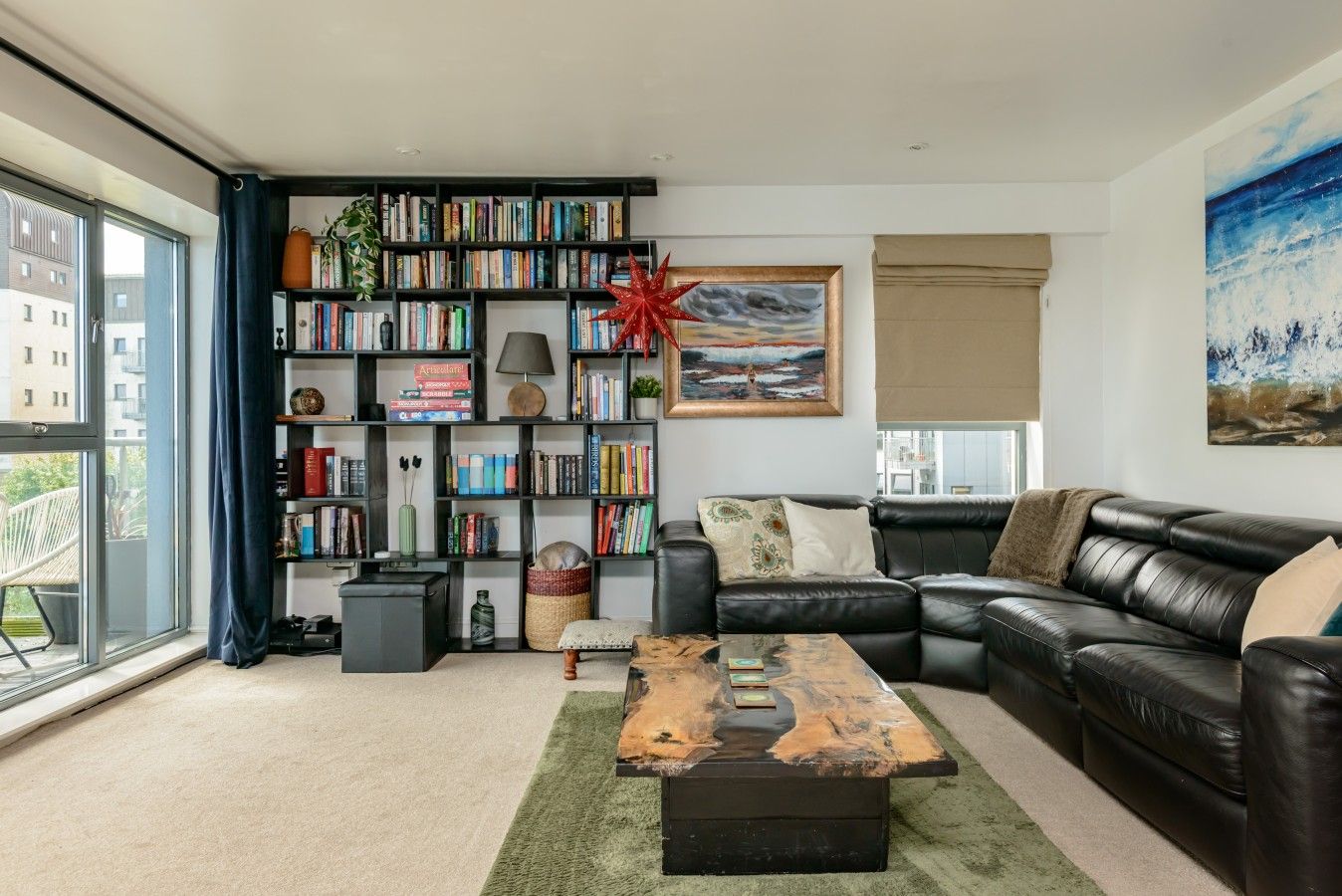Een moderne woonkamer met een leren bank, een boekenkast, een salontafel en een groot raam.