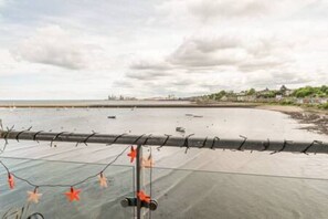 A coastal view with a barbed wire fence, string lights, and a beach in the background.