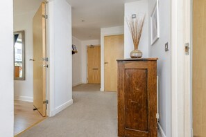 A hallway with wooden doors, a mirror, and a vase on a cabinet. - Calming Sea View City Apartment (Edinburgh)