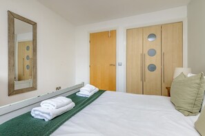 A hotel room with a bed, a mirror, a wardrobe with circular cutouts, and a green towel on the floor.