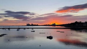 A sunset over a calm harbor with boats and a distant city skyline. - Calming Sea View City Apartment (Edinburgh)