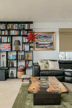 A living room with a bookshelf, a painting, a sofa, and a coffee table. - Calming Sea View City Apartment (Edinburgh)