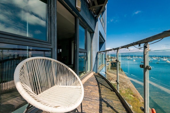 A balcony with a wicker chair, glass doors, and a view of a marina with boats. - Calming Sea View City Apartment (Edinburgh)