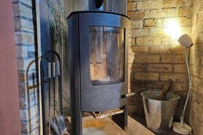 Een kamer met een houtkachel, een metalen emmer en een muur met een baksteenmotief.
