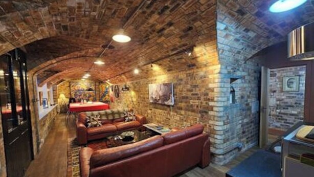 A cozy lounge area with a brick wall, a leather sofa, and a small table. - The Armoury: Stylish WW1 Bunker (North Queensferry)
