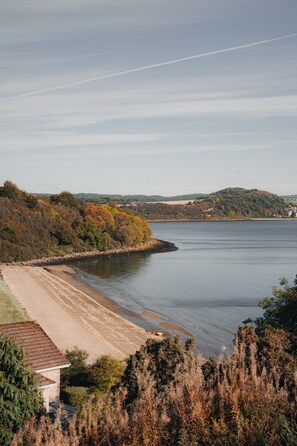 Un paysage côtier avec une plage de sable, un mur de pierre et un bâtiment doté d’un toit en pente.