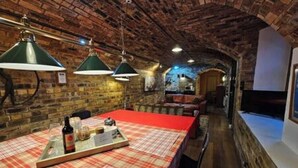 A cozy restaurant with a brick interior, a long table with a red tablecloth, and hanging green lamps. - The Armoury: Stylish WW1 Bunker (North Queensferry)