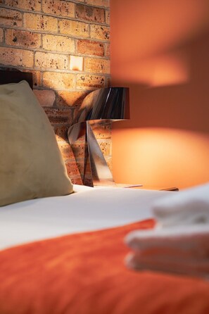 A room with a brick wall, a bed with white bedding, and a lamp.