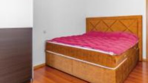 A small bedroom with a wooden bed frame, a wooden headboard, and a pink bedspread. - Three Bedroom Apartment with Balcony and Sea View (Crikvenica)