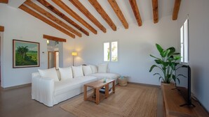 Una sala de estar con sofá blanco, mesa de centro de madera y una planta grande.