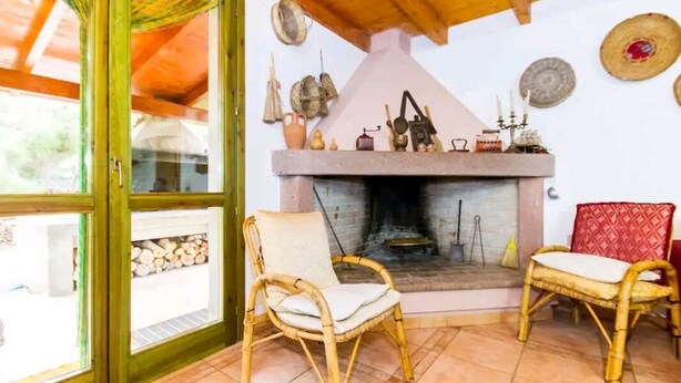 A cozy room with a fireplace, wicker chairs, and a view through a glass door. - Cottage surrounded by greenery ideal for families (SANT'ANTIOCO)