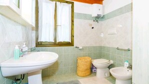 A bathroom with a sink, toilet, bidet, and a window with curtains. - Cottage surrounded by greenery ideal for families (SANT'ANTIOCO)
