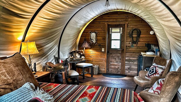 Ein gemütliches Zelt mit Holzvertäfelung, das ein Bett, Stühle, einen Tisch und eine kleine Küchenzeile beherbergt.