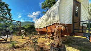 Ein beladener Wagen mit weißem Verdeck, Holzrädern und einer Holzkonstruktion mit einer Tür.