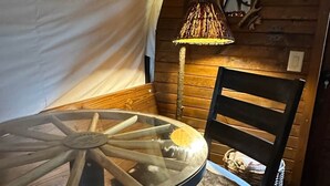 Ein runder Glastisch mit Holzboden, eine gewebte Lampe, ein Holzstuhl und eine rustikale Wand mit einem Spiegel.