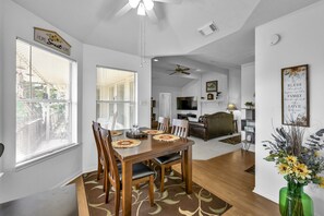 Un coin repas avec une table et des chaises en bois, un ventilateur de plafond et une vue sur le salon.
