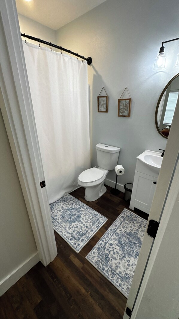 Un baño con cortina de ducha, inodoro, lavamanos y dos cuadros en la pared.