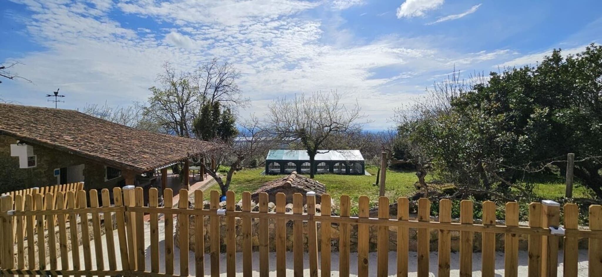 A rustic building with a tiled roof, a wooden fence, and a clear sky.