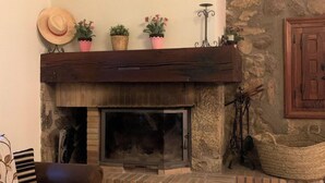A cozy living room with a stone fireplace, a wooden mantel, and a stone wall. - Casa Rural (Candeleda)