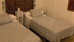 A room with two beds, a wooden headboard, a bedside table with a lamp, and a hanging light fixture. - Casa Rural (Candeleda)