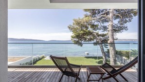 En balkon med trægulv, to loungesenge og havudsigt samt fjerne bakker.