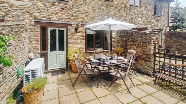 A stone house with a patio table set for dining, a white umbrella, and a gate. - Discover a cosy two-bedroom cottage on the Colmer Estate in Ivybridge. (Ivybridge)