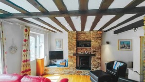 A living room with a stone fireplace, wooden beams, red leather sofas, and a television. - Discover a cosy two-bedroom cottage on the Colmer Estate in Ivybridge. (Ivybridge)