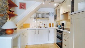 A modern kitchen with white cabinets, a central island, and a built-in oven. - Discover a cosy two-bedroom cottage on the Colmer Estate in Ivybridge. (Ivybridge)