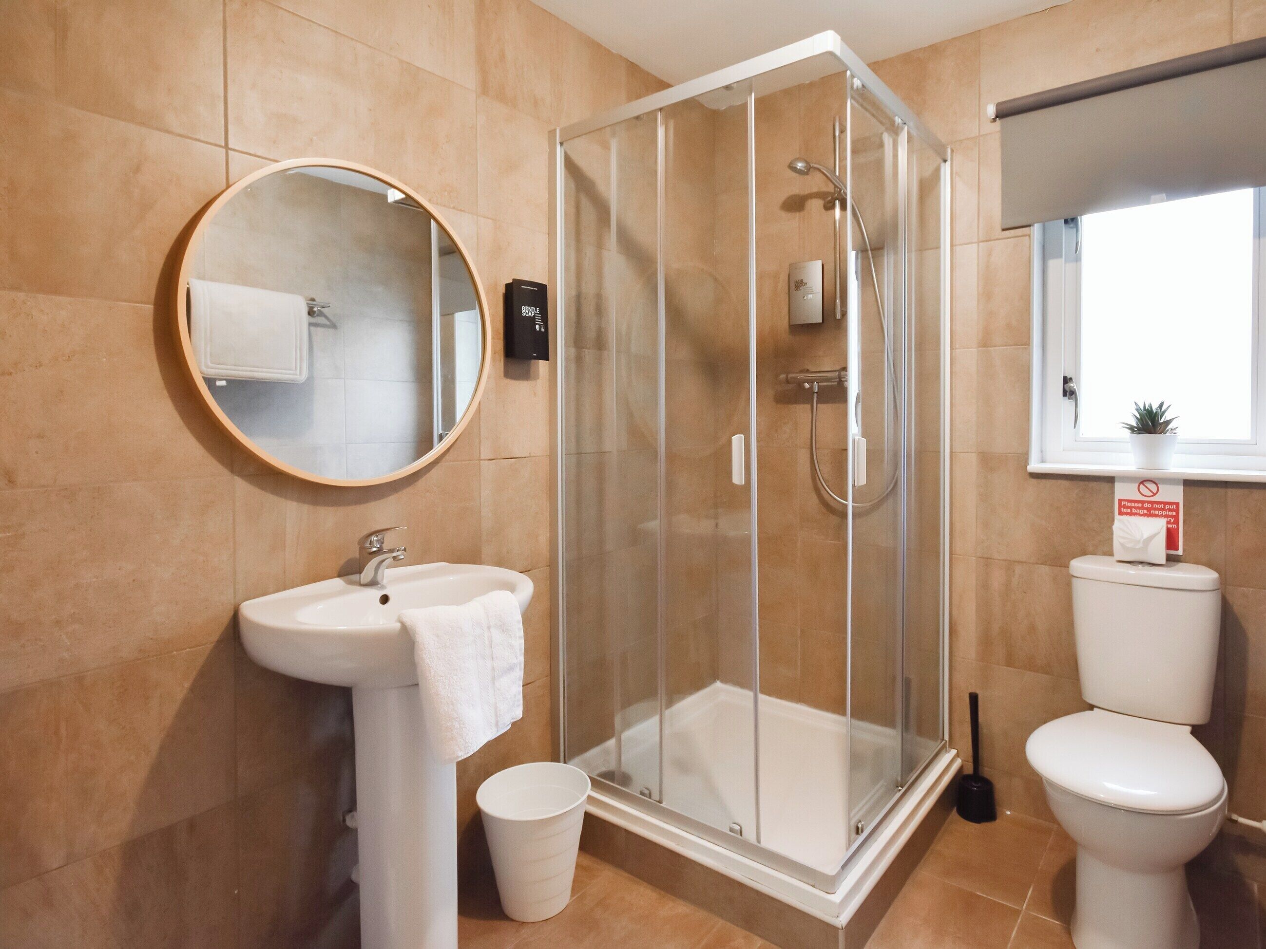 Un baño moderno con ducha envuelta en vidrio, un espejo redondo, un lavabo y un inodoro.