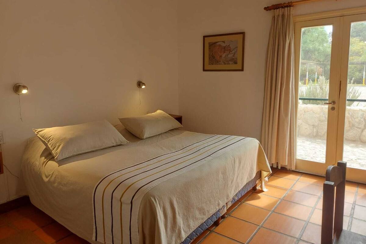 Un dormitori amb un llit, dues làmpades de nit, una porta que dona a zona exterior i un quadre al mur.