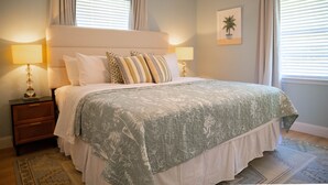 Une chambre à coucher avec un grand lit, deux tables de chevet avec des lampes, une plante fixée au mur et une fenêtre avec des stores.