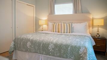 Un dormitorio con una cama grande, dos lámparas de noche, una ventana con cortinas y una puerta.