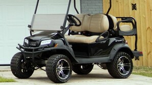 Un véhicule de golf noir avec des sièges de couleur beige est garé devant un garage.