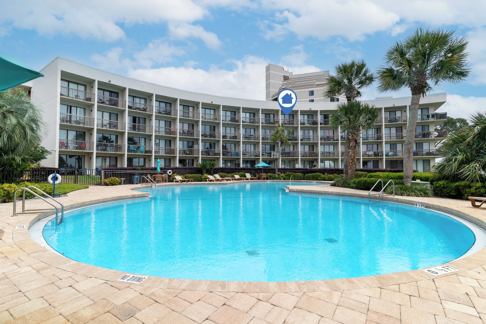 A hotel with a large pool, multiple balconies, and palm trees.