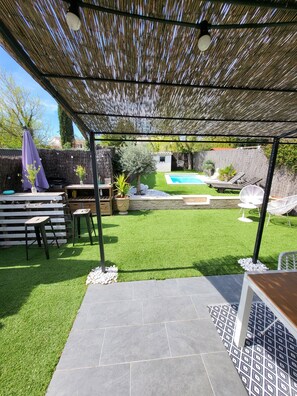 Un patio couvert avec une piscine, du gazon synthétique et du mobilier d’extérieur.