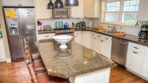 Een keuken met witte kasten, een granieten aanrecht, een roestvrijstalen koelkast, een fornuis en een vaatwasser.