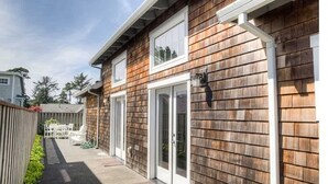 Een tweelaags huis met een houten gevel, witte sierlijsten en een overdekte patio met tuinmeubels.