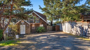 A two-story wooden cabin with a gravel driveway and a wooden fence. - Sea Cliff by Manzanita Beach Getaway: Hot Tub, Stunning Views, Allergen-Free (Manzanita)