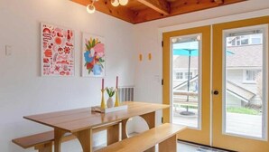 Un comedor con una mesa de madera y bancos, dos obras de arte en la pared y una puerta que da al exterior.