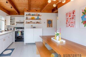 A modern kitchen with white cabinets, wooden countertops, and a wooden dining table with benches. There are decorative items on the shelves and wall art. - Private Idaho by Manzanita Beach Getaway: Hot Tub, Dog-Friendly & Near Beach (Manzanita)