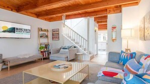 Una sala de estar moderna con techo de madera, una escalera y un cuadro de arte con temática playera.