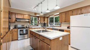 Een moderne keuken met houten kastjes, roestvrijstalen apparatuur, een groot eiland met een spoelbak en hangende lampen.
