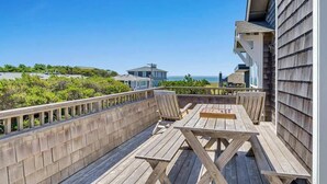 A wooden deck with a table and chairs, overlooking a scenic view of the ocean and hills.