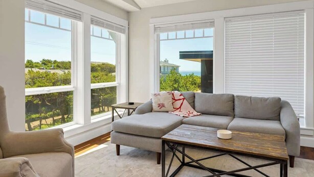 A modern living room with a sectional sofa, a coffee table, and large windows offering a view of greenery and a building.