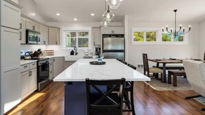A modern kitchen with white cabinets, a large island, and a dining area with a chandelier.